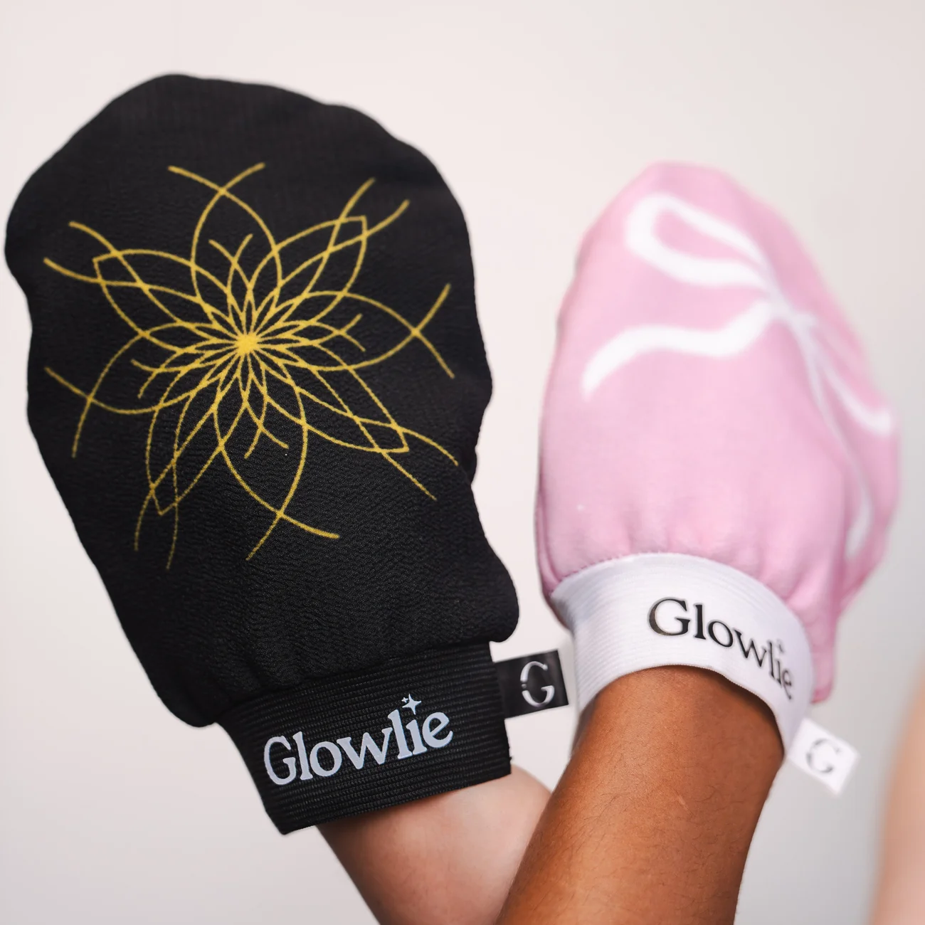 De zwarte en roze Glowlie exfoliatiehandschoen in de hand
